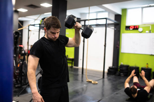 A strong young man is doing dumbbell snatches at the gym